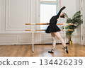 Young ballerina in tutu skirt stretching practicing ballet positions dancing near ballet barre in dance class. Young classical dancer woman in dance studio. Ballet class training Ballet school concept 134426239