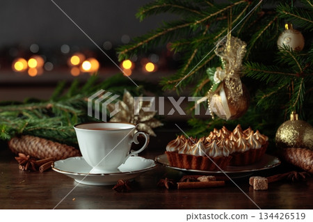 White cup of tea and meringue tartlet on table with Christmas decorations. 134426519