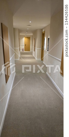 Long corridor with beige walls and wooden doors leading to rooms 134426586