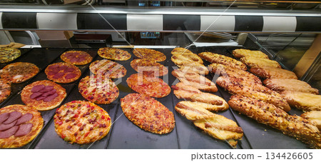 Assorted freshly baked pizzas and breadsticks displayed in bakery 134426605
