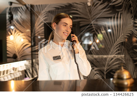 Receptionist talking on the phone while arranging accommodation for the customer Receptionist talking on the phone while arranging accommodation for the customer 134426625