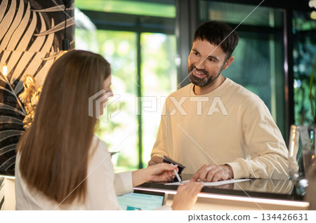 Receptionist talking to a male customer and arranging accommodation for him Receptionist talking to a male customer and arranging accommodation for him 134426631