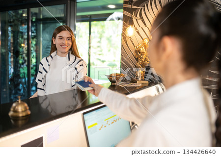 Receptionist arranging accommodation of new visitor and taking passport 134426640