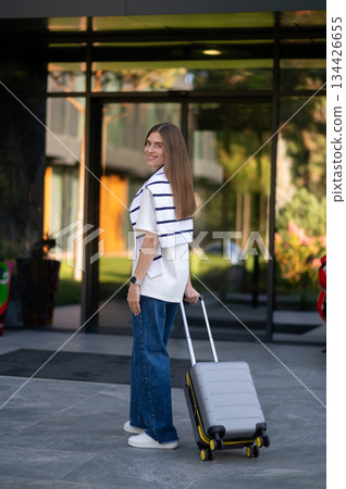Long-haired cute young woman with a suitcase near the hotel Long-haired cute young woman with a suitcase near the hotel 134426655