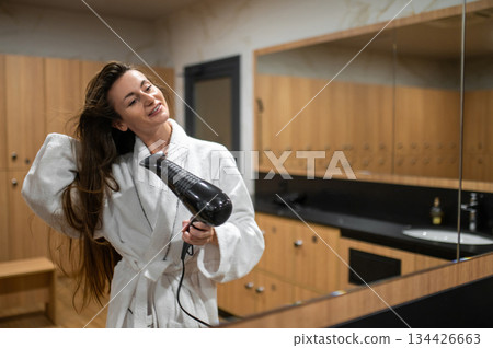 Long-haired caucasian young woman in white robe drying her hair 134426663