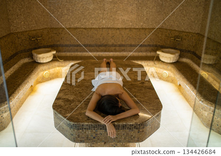 Pretty young woman in white towel on a massage table in a spa center Pretty young woman in white towel on a massage table in a spa center 134426684