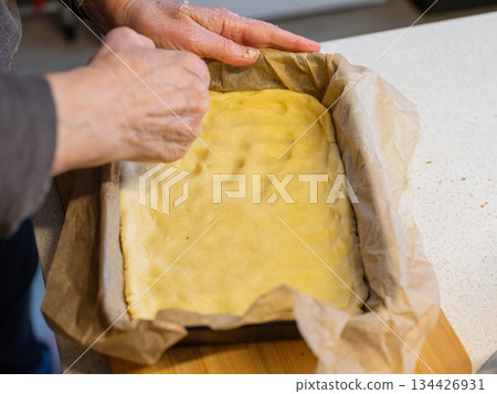Hands preparing dough in baking dish for delicious homemade dessert Hands preparing dough in baking dish for delicious homemade dessert 134426931