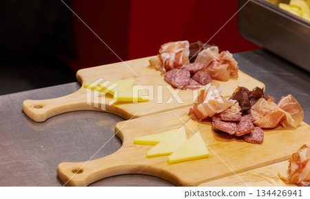 Assorted cured meats and cheese on wooden cutting boards in kitchen Assorted cured meats and cheese on wooden cutting boards in kitchen 134426941
