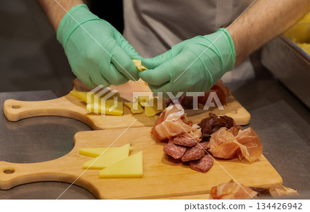 Culinary expert preparing assorted meats and cheeses on wooden cutting boards 134426942