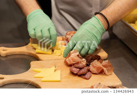 Culinary expert preparing assorted meats and cheeses on wooden cutting boards Culinary expert preparing assorted meats and cheeses on wooden cutting boards 134426943
