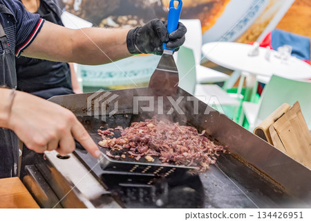 Chef grilling meat on flat top griddle in busy outdoor kitchen setting 134426951