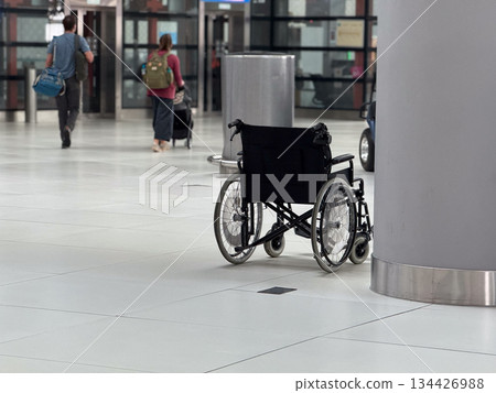 Empty wheelchair placed near column inside airport terminal hall. Mobility assistance availability, accessibility awareness, inclusive transport services, and support infrastructure concept. Empty wheelchair placed near column inside airport terminal hall. Mobility assistance availability, accessibility awareness, inclusive transport services, and support infrastructure concept. 134426988
