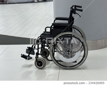 Side view of empty wheelchair standing in airport terminal hall. Inclusive transportation concept, mobility assistance availability, accessibility awareness, and support for passengers. 134426993