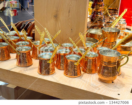 Turkish Copper cezve coffee pots arranged on wooden shelf in souvenir shop. Traditional coffee preparation, metal craftsmanship, cultural ritual, hospitality heritage, artisanal cookware and retail 134427006