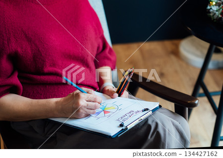 Woman drawing work-life balance wheel sitting on armchair at cozy dark home interior. Self-reflection, life planning for next new year. Personal Year review. Coaching tools. Finding Balance in Life 134427162
