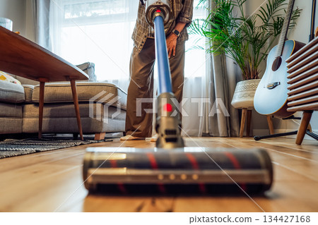 Focus on close up cordless vacuum cleaner vacuuming wooden floor of modern apartment living room with green plants. Daily routine and household chores. Housekeeping, home cleaning concept Focus on close up cordless vacuum cleaner vacuuming wooden floor of modern apartment living room with green plants. Daily routine and household chores. Housekeeping, home cleaning concept 134427168