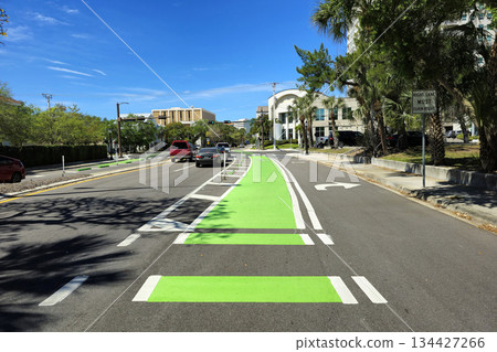 Marked green bike lane on Sarasota city street, passing vehicles and urban scenery. Sustainable transit and road-sharing infrastructure in Florida Marked green bike lane on Sarasota city street, passing vehicles and urban scenery. Sustainable transit and road-sharing infrastructure in Florida 134427266