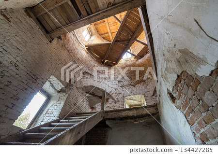 Large spacious forsaken empty basement room of ancient building or palace with cracked plastered brick walls, small windows, dirty floor and wooden staircase ladder. 134427285