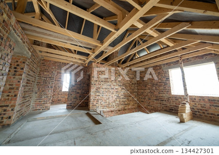 Interior of unfinished brick house with concrete floor, bare walls ready for plastering and wooden roofing frame attic under construction. Interior of unfinished brick house with concrete floor, bare walls ready for plastering and wooden roofing frame attic under construction. 134427301