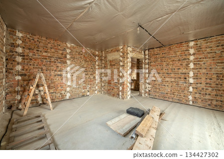 Interior of unfinished brick house with concrete floor and bare walls ready for plastering under construction. Real estate development 134427302