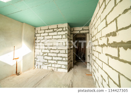 Interior of an apartment room with bare walls and ceiling under construction. 134427305