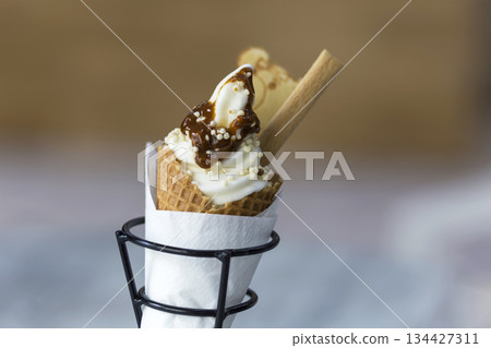 Ice cream dessert in wafer cup with chocolate cookies and creative decoration topping on blurred light copy space background. 134427311