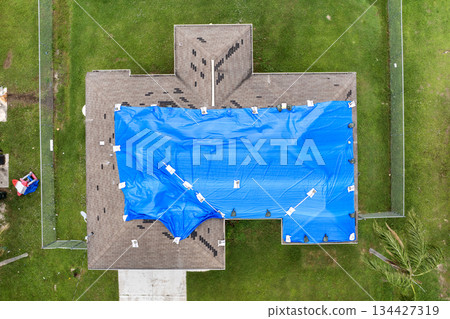 Home rooftop wrapped in plastic tarp following hurricane damage, protecting structure from water penetration until permanent roofing materials are restored 134427319