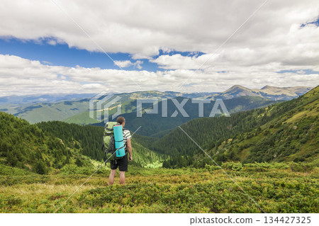 Hiker with a backpack standing in mountains Hiker with a backpack standing in mountains 134427325