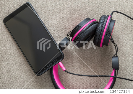 Headphone connected to cellphone isolated on light cloth flat copy space background. Modern technology, trendy entertainment, gadget design and accessories concept. 134427334