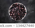 Top view of frozen aronia or black chokeberry berries in white bowl on dark textured background. Healthy food. 134427440