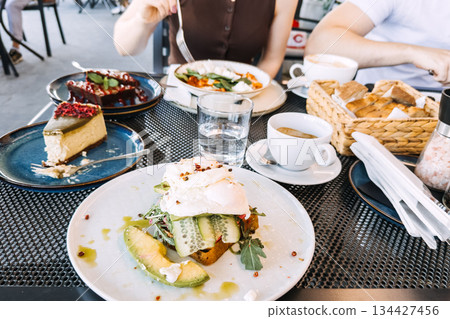 Poached eggs on avocado toast served at outdoor cafe table. Gourmet breakfast, cafe dining, social eating, food aesthetics. Poached eggs on avocado toast served at outdoor cafe table. Gourmet breakfast, cafe dining, social eating, food aesthetics. 134427456
