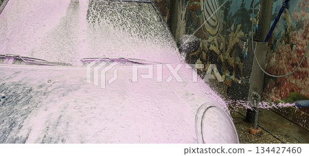 Car wash with pink foam covering vehicle in vibrant outdoor setting 134427460