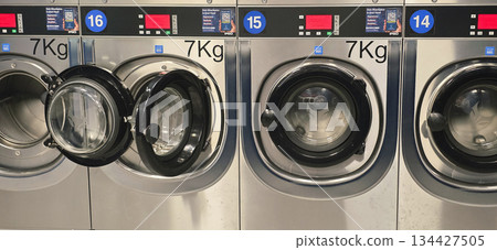 Berlin, Germany - September 25, 2025: Commercial washing machines in laundromat with open door and digital display 134427505