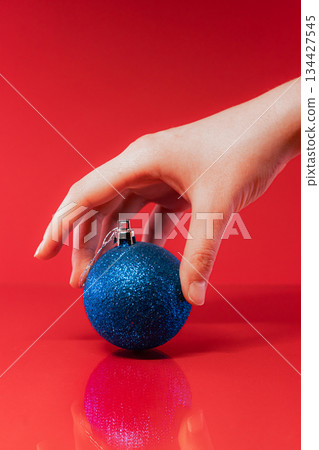 Hand Holding Blue Christmas Bauble on Red Background Hand Holding Blue Christmas Bauble on Red Background 134427545