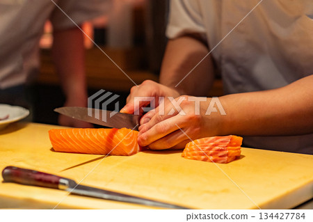 Chef slicing fresh salmon fillet on wooden cutting board in kitchen Chef slicing fresh salmon fillet on wooden cutting board in kitchen 134427784