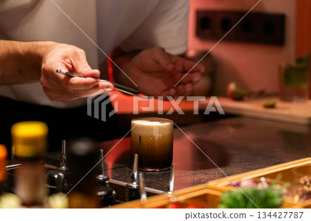 Bartender crafting cocktail with precision in modern bar setting Bartender crafting cocktail with precision in modern bar setting 134427787