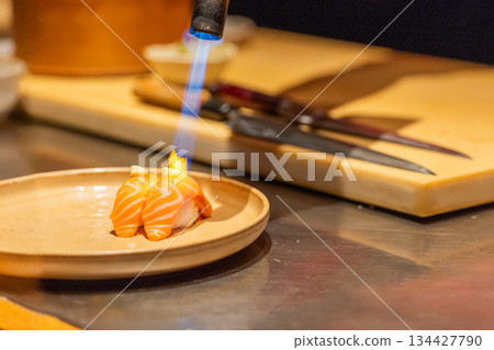 Culinary chef using torch to sear salmon sushi on plate in kitchen 134427790