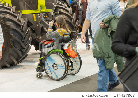 Berlin, Germany - January 21, 2025: Woman in wheelchair photographing tractor at expo Berlin, Germany - January 21, 2025: Woman in wheelchair photographing tractor at expo 134427808
