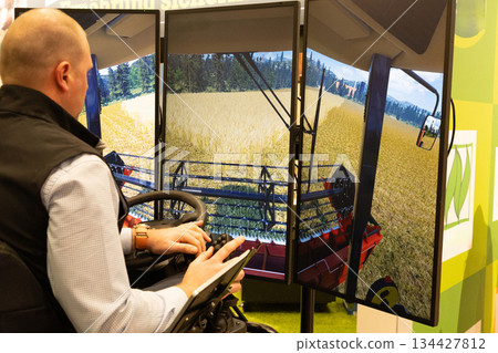 Berlin, Germany - January 24, 2025: Man operating advanced agricultural simulator with immersive screens Berlin, Germany - January 24, 2025: Man operating advanced agricultural simulator with immersive screens 134427812