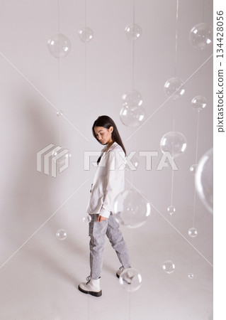 A woman with black hair wakes up in the morning in a white blanket and catches the rays of the sun. The portrait is creative, with brown eyes. High quality photo 134428056