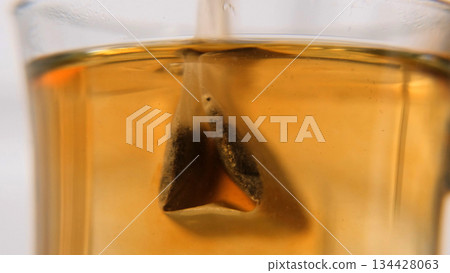 Macro shot of a teabag sinking into hot water, as tea leaves release color. Calm morning ritual and cozy breakfast concept Macro shot of a teabag sinking into hot water, as tea leaves release color. Calm morning ritual and cozy breakfast concept 134428063