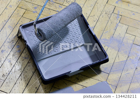 Close-up showcasing a paint roller soaked in gray paint, resting on a paint tray Close-up showcasing a paint roller soaked in gray paint, resting on a paint tray 134428211
