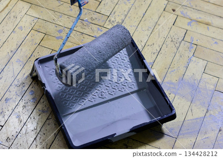 A paint roller and tray filled with gray paint rest on a herringbone wooden floor A paint roller and tray filled with gray paint rest on a herringbone wooden floor 134428212