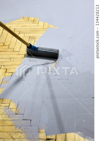 Applying gray paint to a herringbone parquet floor with a paint roller Applying gray paint to a herringbone parquet floor with a paint roller 134428213