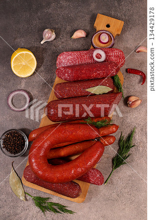 Delicious, aromatic appetizers of various salami cuts for the holidays. A selection of various smoked and dry-cured sausages and spices on a kitchen background. Advertising and menu for a store 134429178