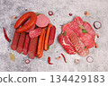 An assortment of various types of sausages, smoked meats, salami, and game sausages with lemon, spices, and herbs on a concrete table. Advertising and banner for a store, menu for a cafe or restaurant 134429183