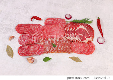 Delicious, aromatic appetizers of various salami cuts for the holidays. A selection of various smoked and dry-cured sausages and spices on a kitchen background. Advertising and menu for a store Delicious, aromatic appetizers of various salami cuts for the holidays. A selection of various smoked and dry-cured sausages and spices on a kitchen background. Advertising and menu for a store 134429192