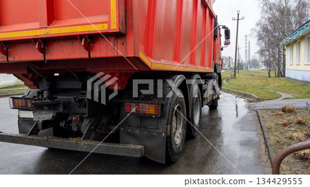 Red dump truck on the side of the road. Construction equipment is parked. The truck is used for transporting bulk materials. 134429555