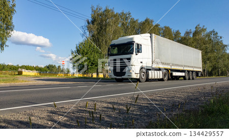 White semi-truck with a fully loaded cargo trailer driving along countryside road. The lorry travels on an empty freeway. White semi-truck with a fully loaded cargo trailer driving along countryside road. The lorry travels on an empty freeway. 134429557