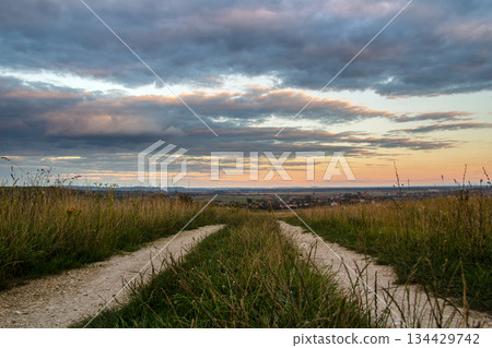 Dirt road among dark fields at sunset with dramatic cloudscape. 134429742